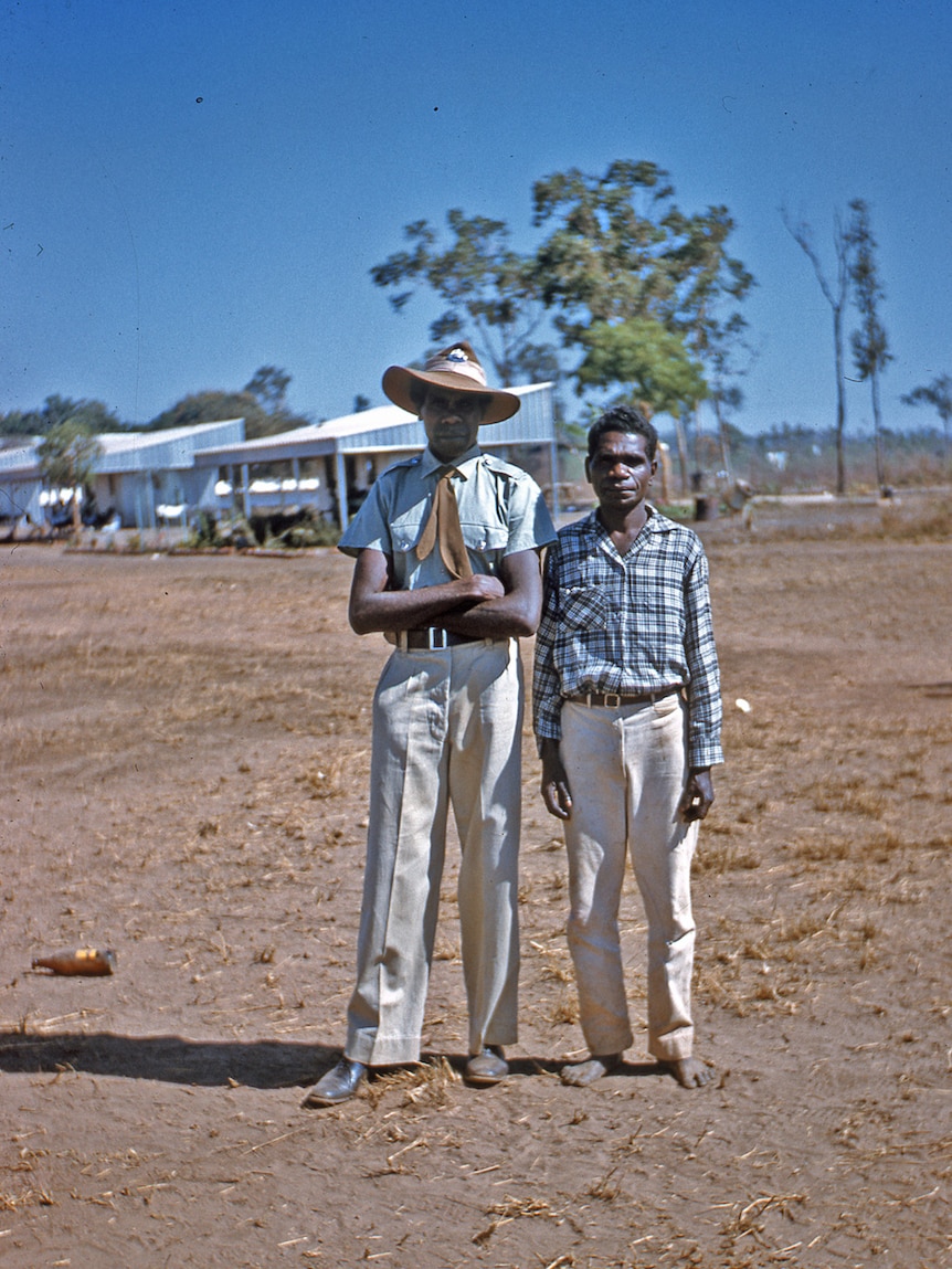 A photo of two well-dressed police trackers standing in a dusty field in the Northern Territory in the 1950s.