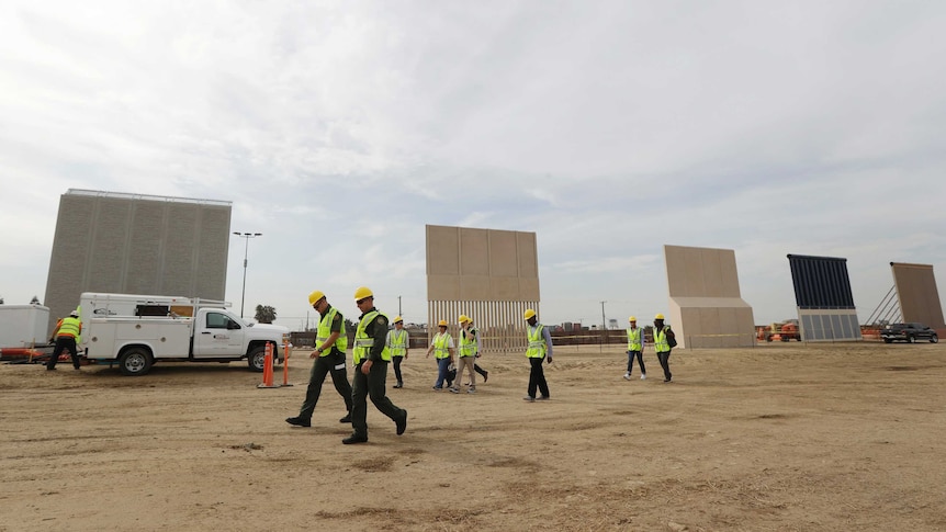 Workers in hard hats walk pass the border wall prototypes.