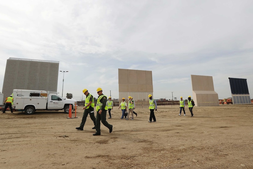 Workers in hard hats walk pass the border wall prototypes.