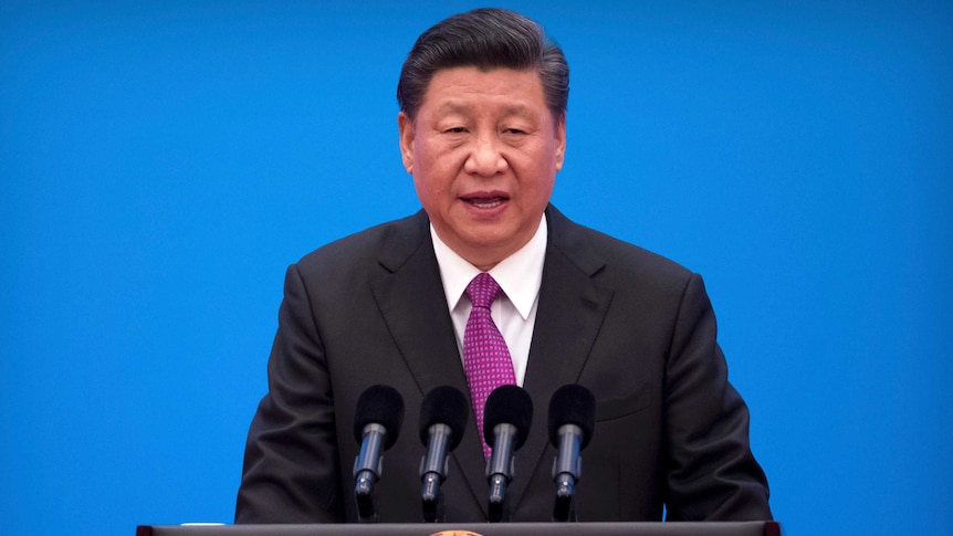 Chinese President Xi Jinping speaks at a podium with microphones in front of a blue background