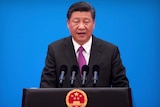 Chinese President Xi Jinping speaks at a podium with microphones in front of a blue background