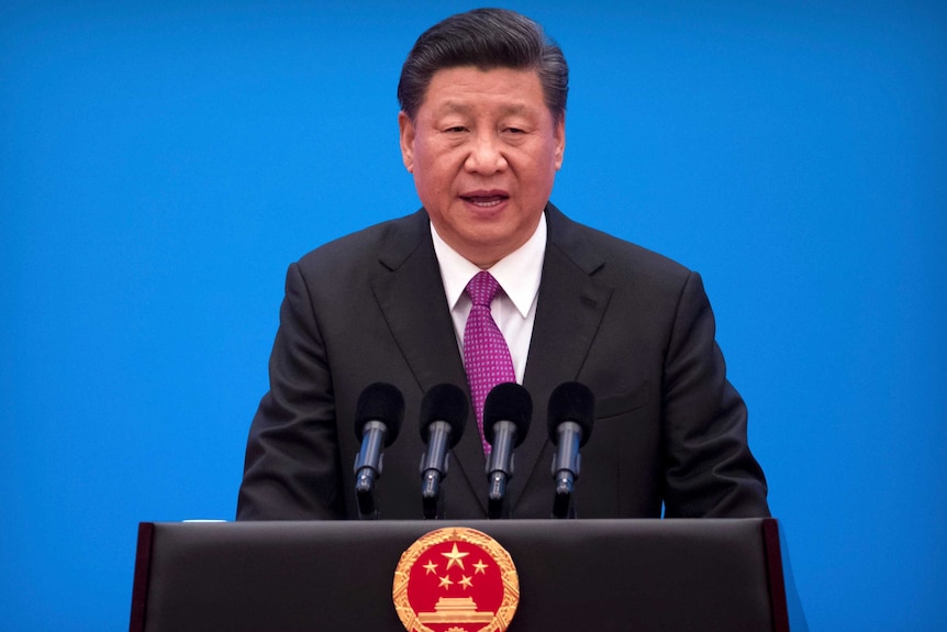 Chinese President Xi Jinping speaks at a podium with microphones in front of a blue background