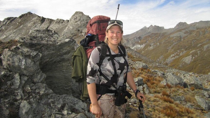 A woman on standing on the top of a rocky mountain range with a pack on her back.
