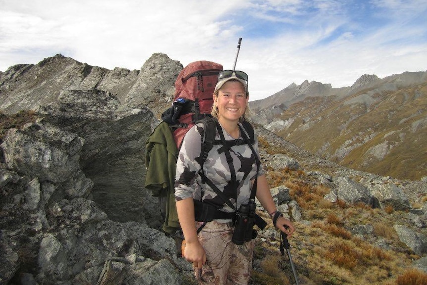A woman on standing on the top of a rocky mountain range with a pack on her back.