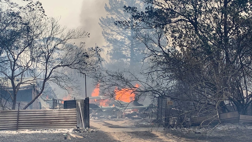 Smoke and flames rise from charred wreckage and twisted metal where a house once stood.