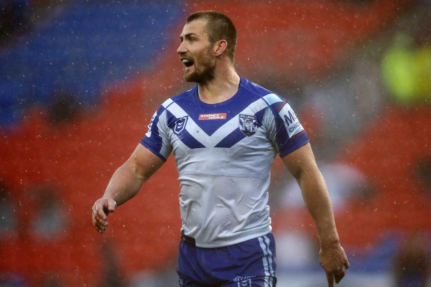 An NRL player stands in the rain, looking down the field and shouting.