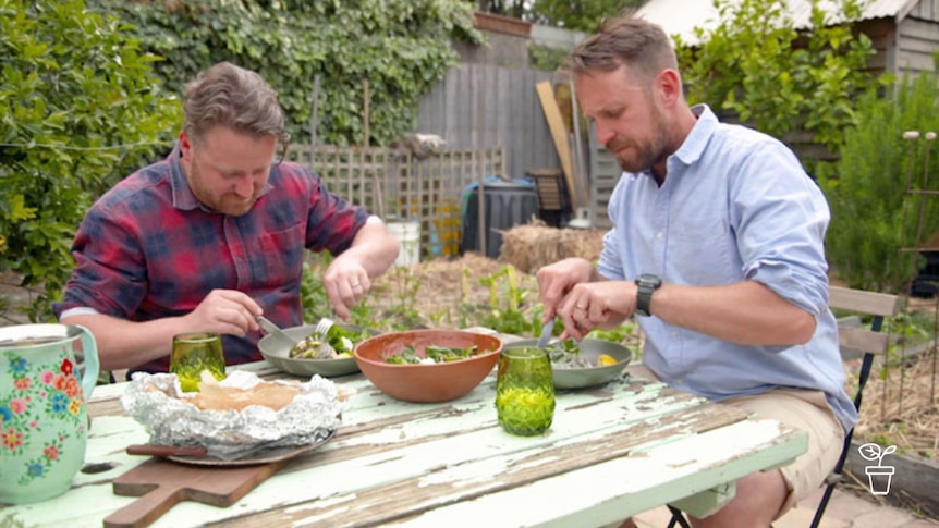 Two men eating a meal at a table in a garden