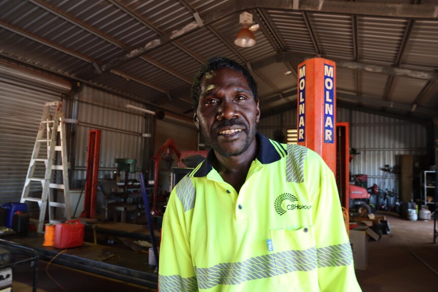 A man in a high-vis shirt standing inside a warehouse and smiling.