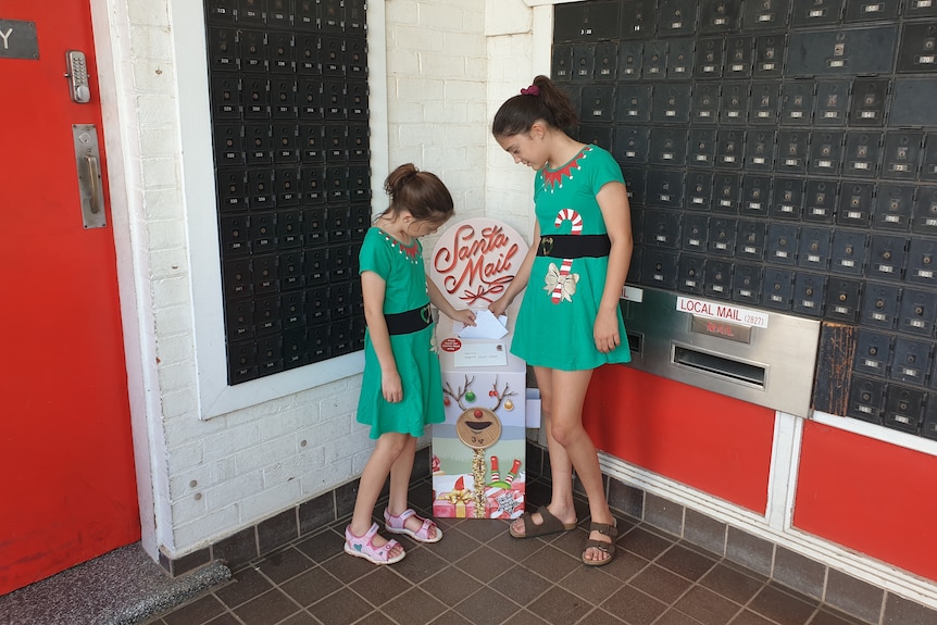 Two young girls stand in front of a post box for Santa letters