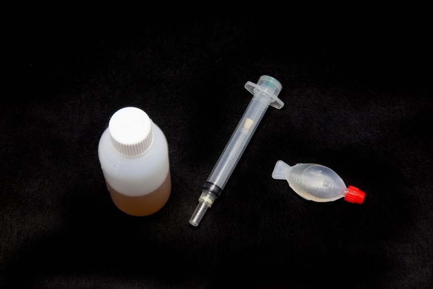 A bottle, plastic syringe, and small soy sauce container against a black background.