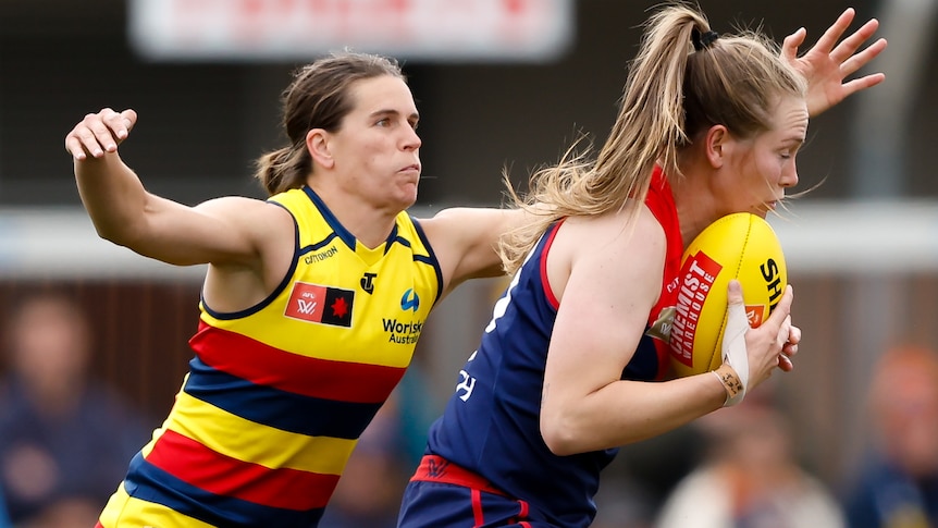 An Adelaide Crows AFLW player attempts to tackle a Melbourne opponent.