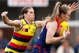 An Adelaide Crows AFLW player attempts to tackle a Melbourne opponent.