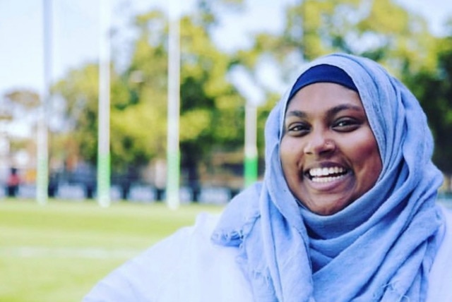 A woman wearing a hijab looks at the camera and smiles.