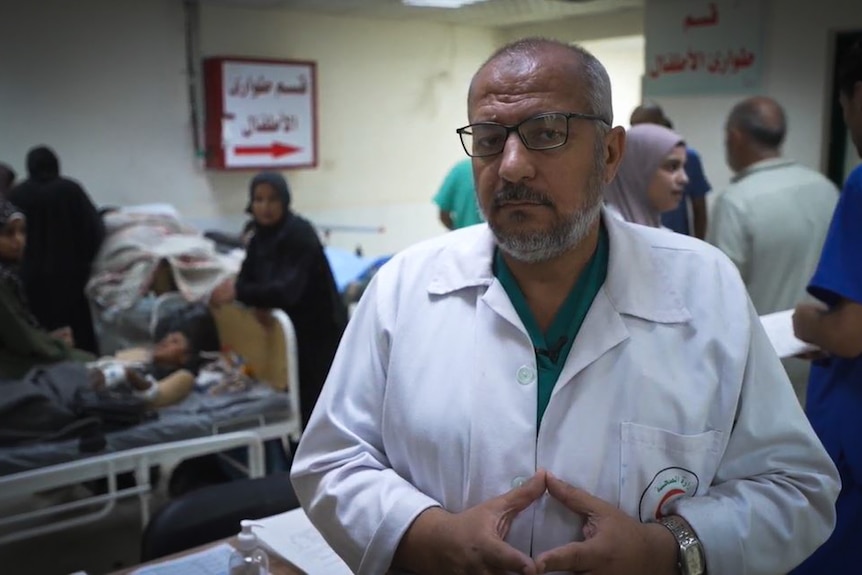 A close up of a doctor wearing a white coat in a hospital ward.