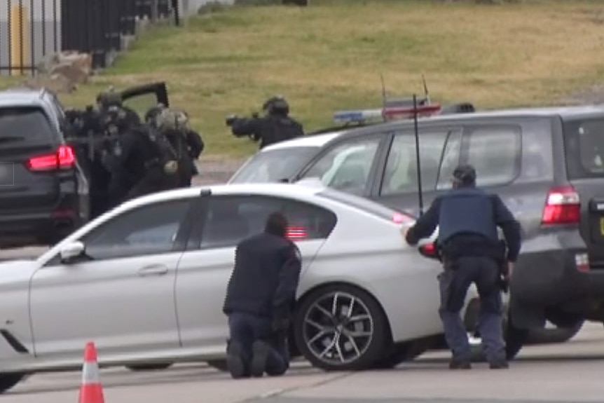 police some holding rifles and others crouching behind cars attend a siege situation in a town in new south wales