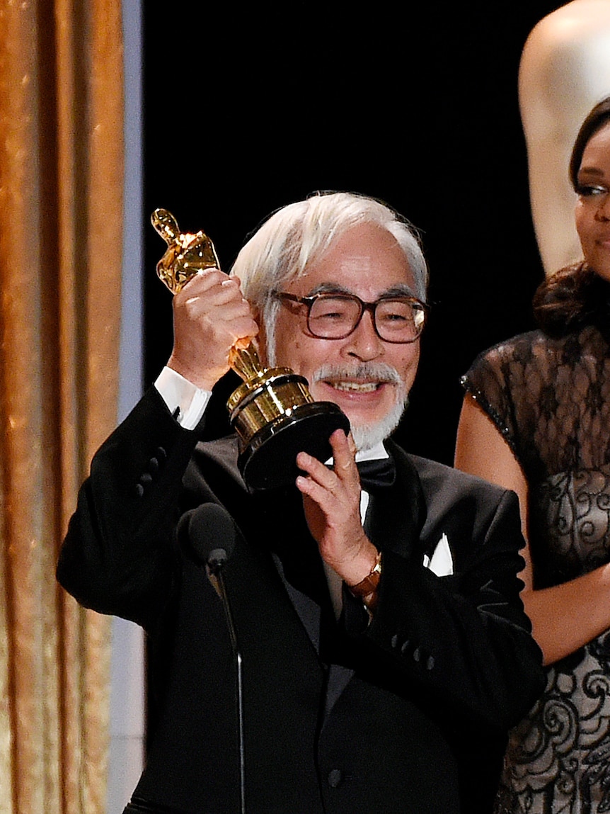 Hayao Miyazaki holds up an Oscar statue on stage at hte academy awards 