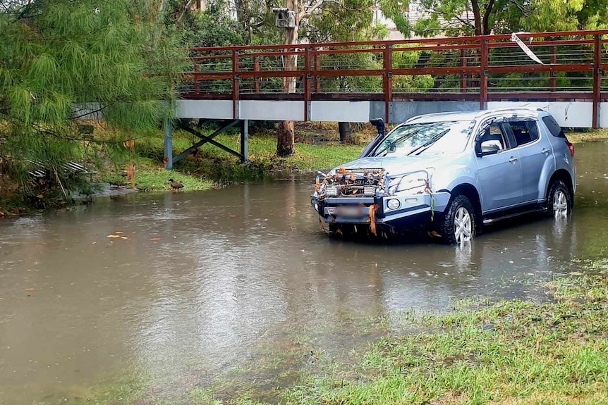 A blue car sitting in water in a creek in Elwood.