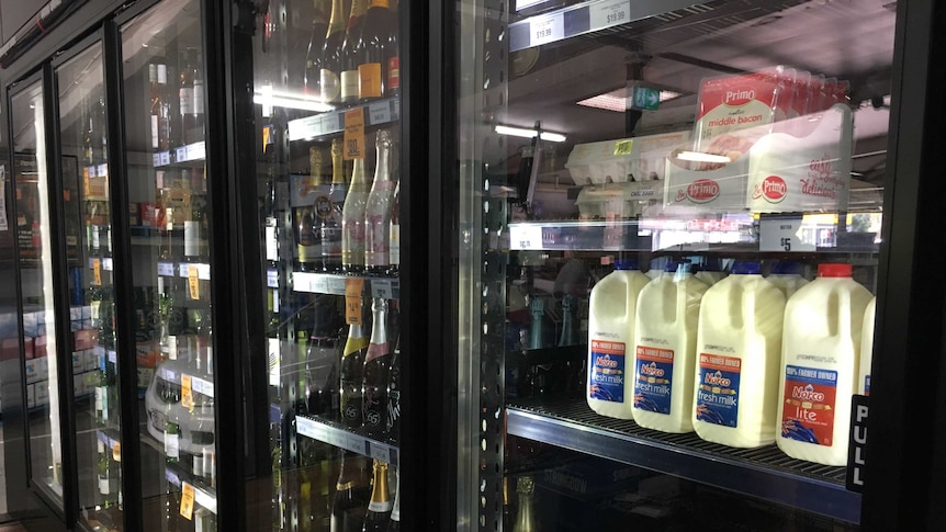 Milk, bacon and eggs is stacked on a shelf next to wine bottles in a fridge at a bottle shop.