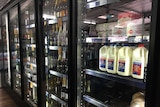 Milk, bacon and eggs is stacked on a shelf next to wine bottles in a fridge at a bottle shop.