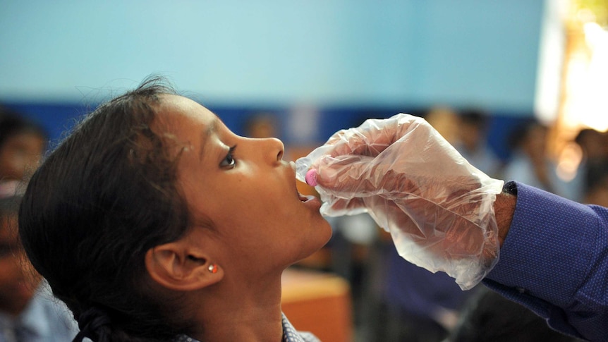 A child opens her mouth to receive a pill from a gloved hand in a school environment