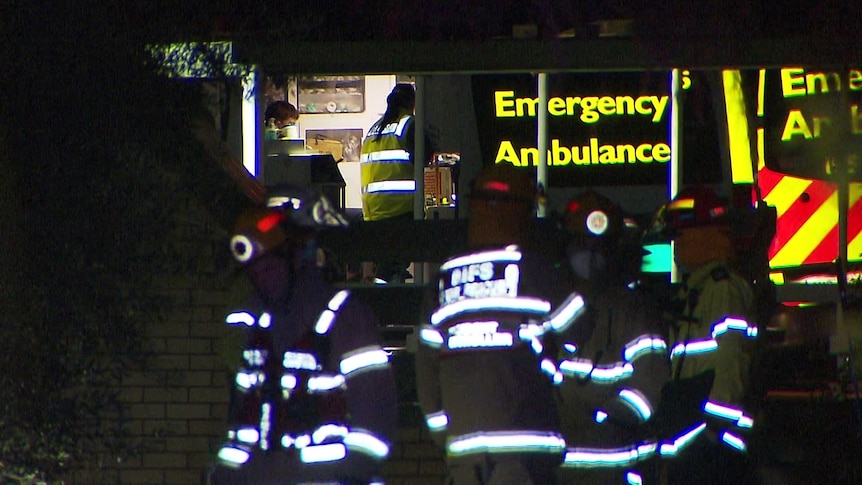 An ambulance with its door open and a patient inside with three fire fighters in the foreground