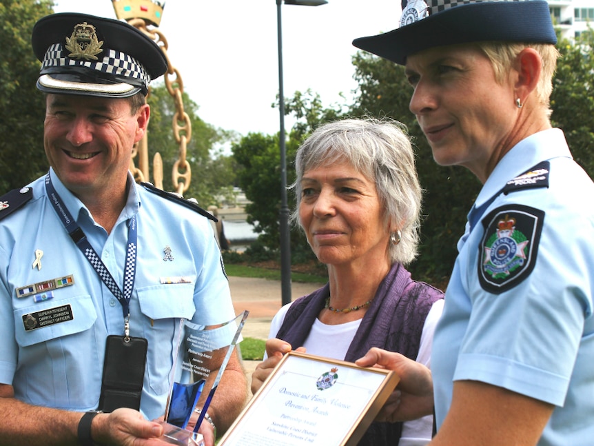 Two police officers and another lady holding awards in a staged photo.