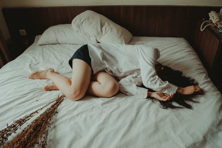 An unidentified woman lays on an unmade bed.