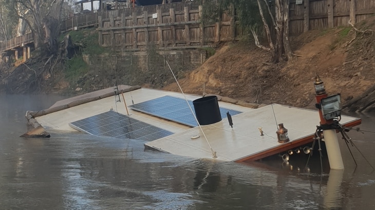 top of boat visible while the rest is under water along the bank of a river
