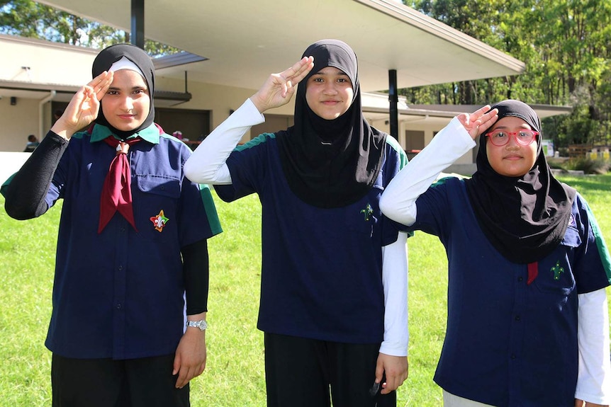 Three Muslim scouts standing in front of a building doing the scout salute