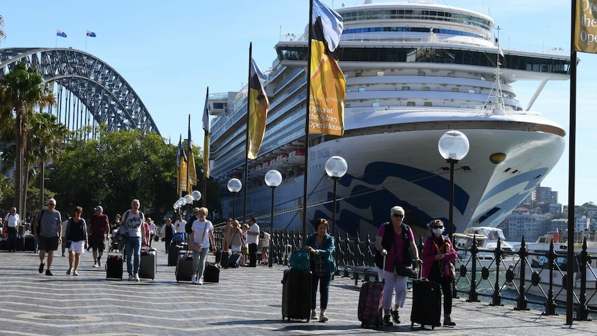 Plusieurs personnes passant devant un grand navire, le pont du port de Sydney étant visible en arrière-plan