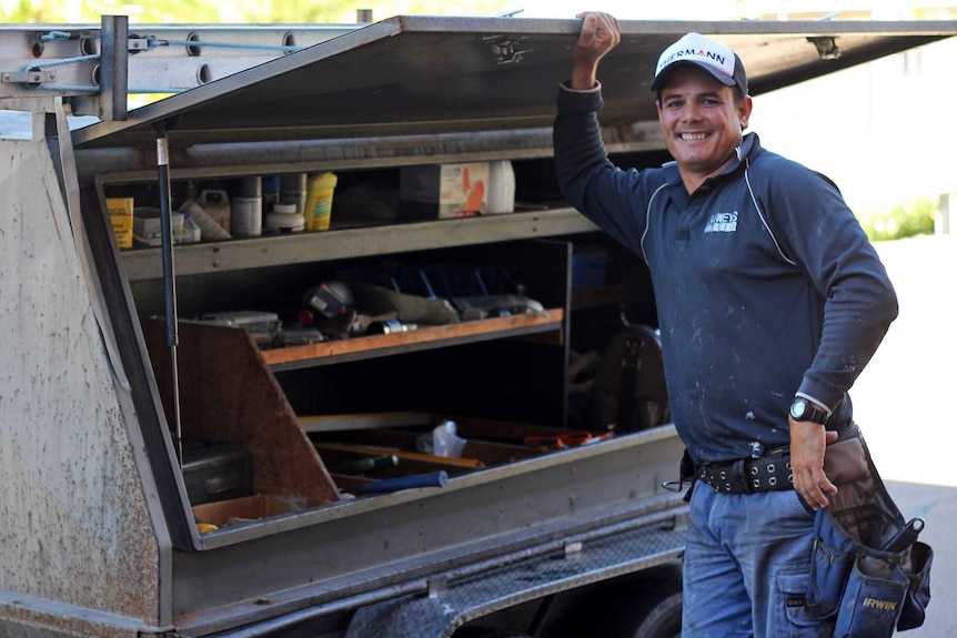 Tradesman Darcy Rowe stands beside his trailer of tools smiling