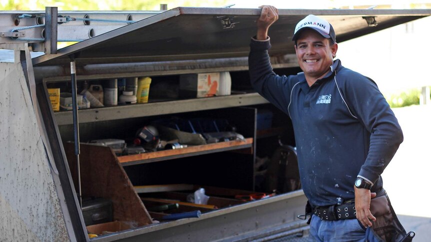 Tradesman Darcy Rowe stands beside his trailer of tools smiling