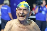 George Corones smiles to crowd in swimming cap and goggles.