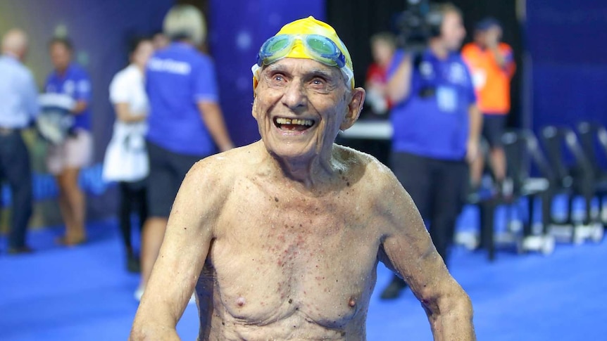 George Corones smiles to crowd in swimming cap and goggles.