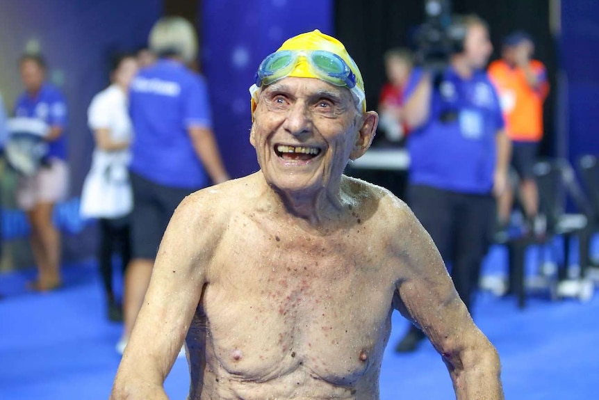 George Corones smiles to crowd in swimming cap and goggles.
