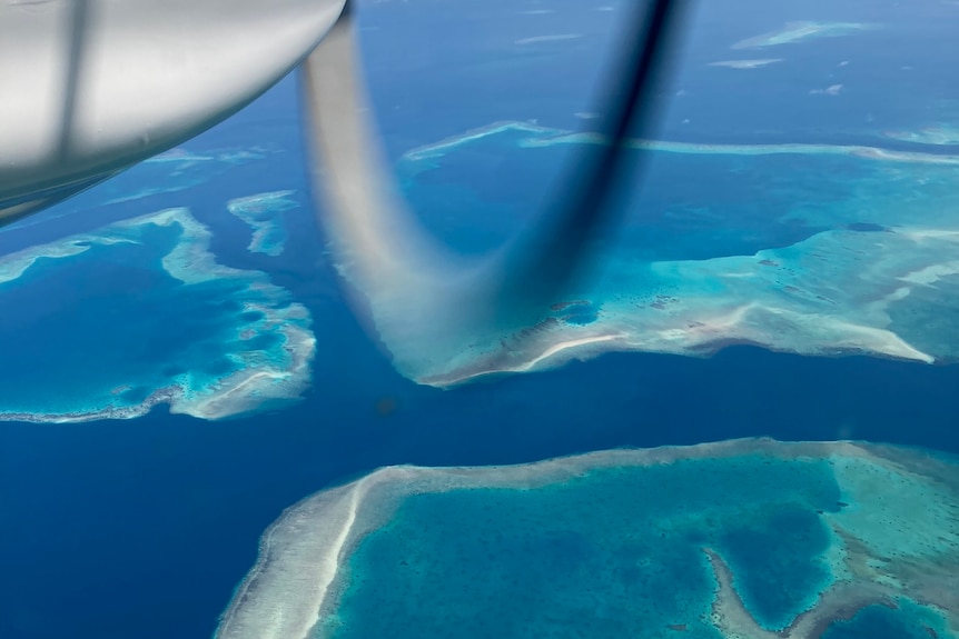 An aerial view of deep blue ocean with circles of lighter blue within it. Light plane propeller is just visible. 