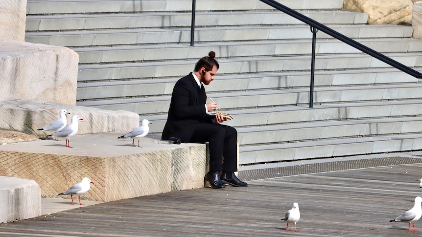 A lone man eats lunch during COVID-19 lockdown at Barangaroo in Sydney, while seagulls look on..