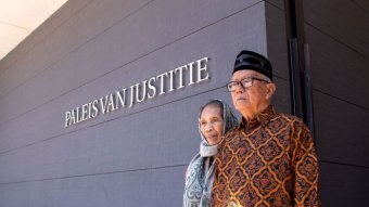 An elderly Indonesian man and woman stand outside a courtroom.