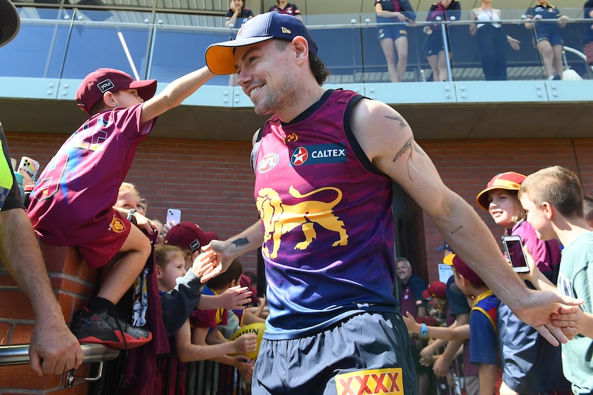 lachie neale enters the training field surrounded by fans smiling