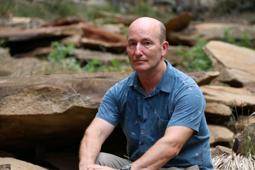 A man standing on the edge of a creek surrounding by red stones.