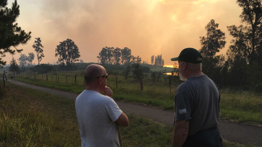Two men look at an orange smoky sky caused by fires near Newcastle Airport