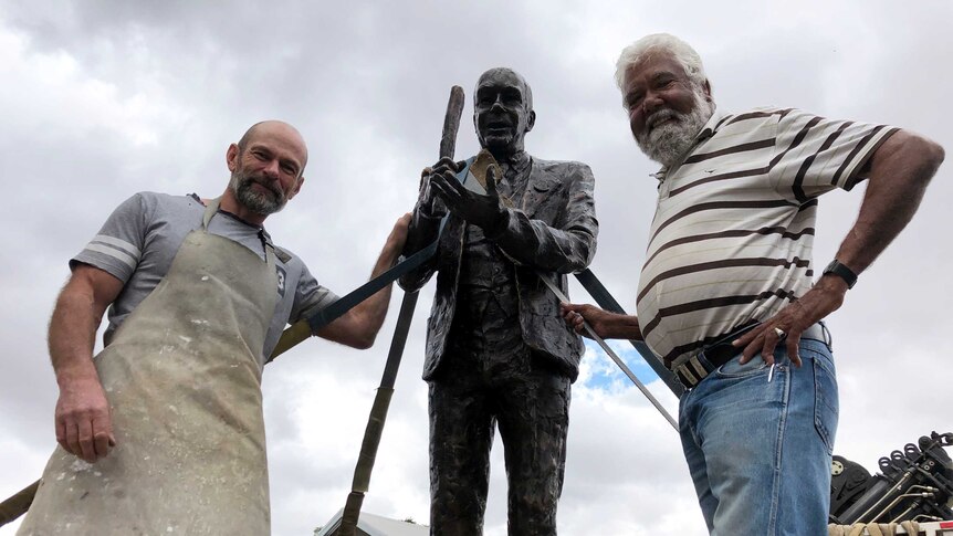 Two men stand alongside a bronze sculpture.