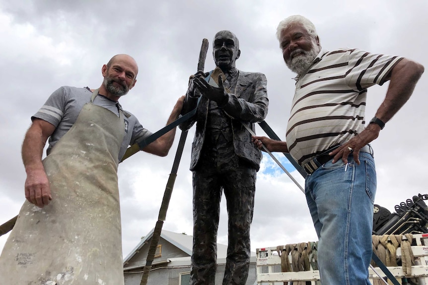 Two men stand alongside a bronze sculpture.