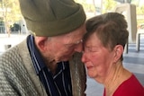 An older man and a woman hug tearfully.