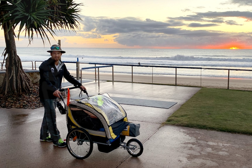 A man pushes a hand cart along a path in front of the beach at sunrise. 
