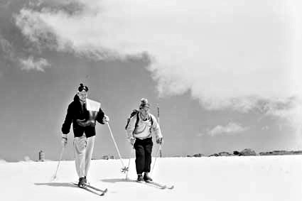 Old black and white photograph shows two men in 1950s ski gear on the snow.