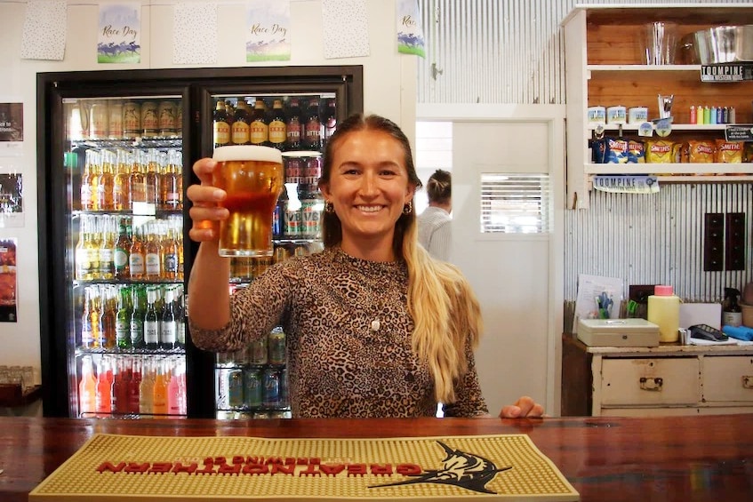 Becky holds up a beer from behind the bar