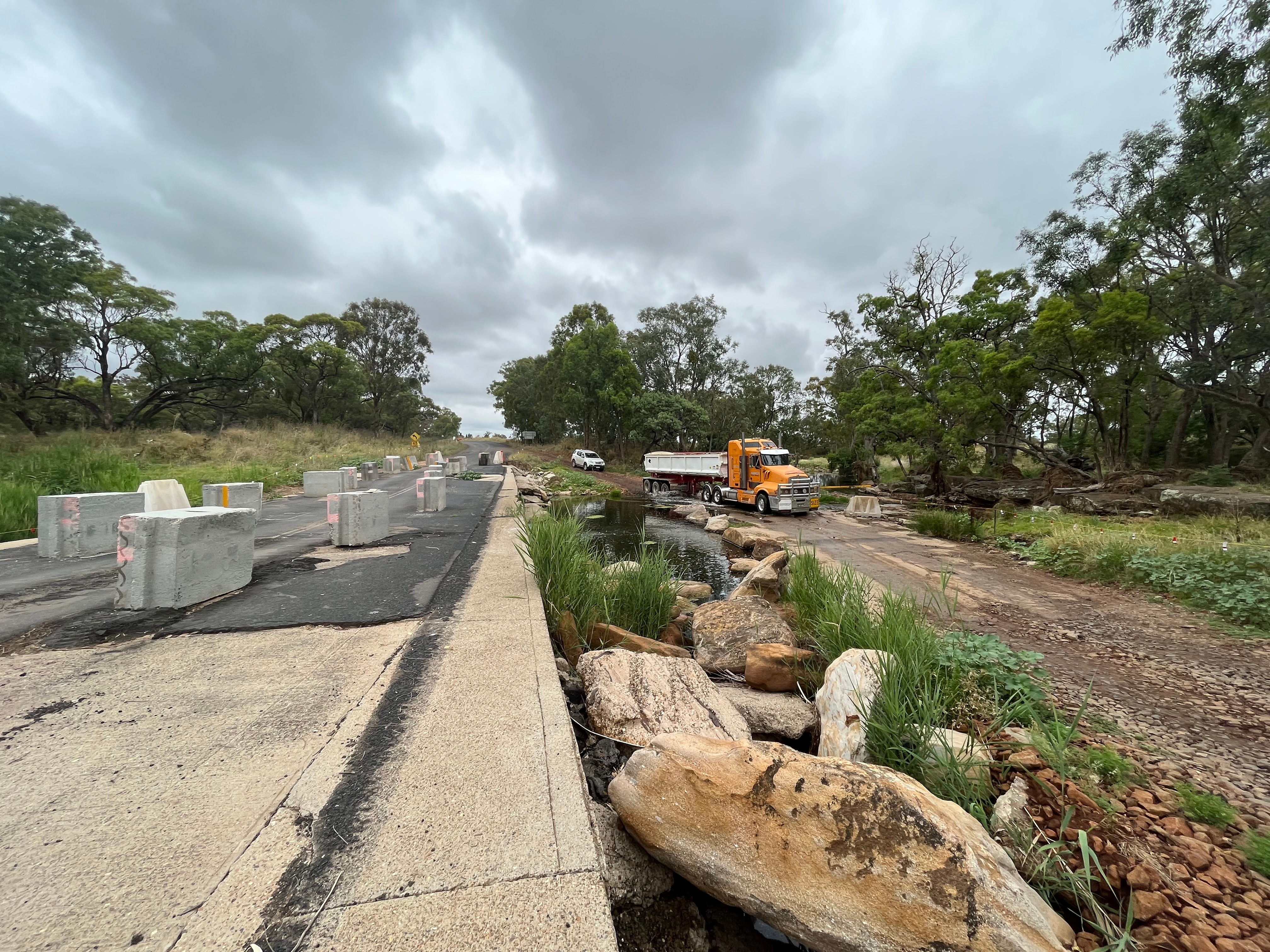 A truck drives through a creek and around a damaged causeway
