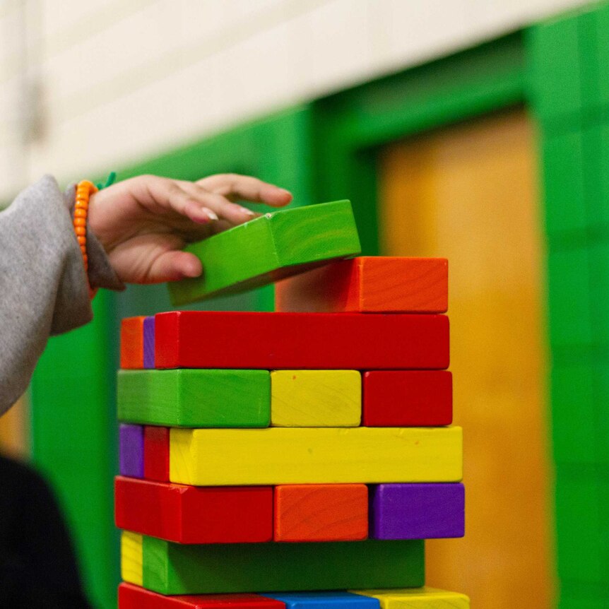 structure made of kid's coloured wooden blocks with child's hand placing one block on the top