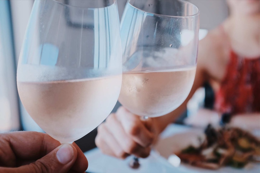 Close-up of two people's hands toasting with glasses of wine.